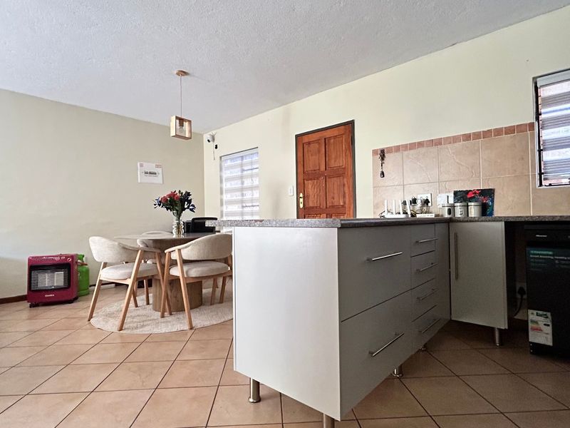 Open-plan living and kitchen area featuring tiled flooring, modern cabinetry with stone countertops, and a tiled backsplash, creating a functional and cohesive living space.