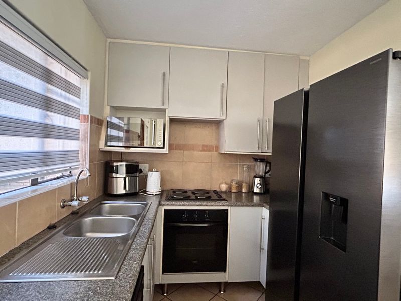 Compact kitchen featuring granite countertops, a double bowl stainless steel sink, built-in oven, hob, and neutral cabinetry with tiled backsplash.