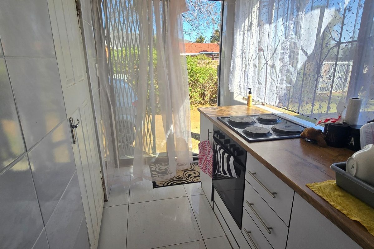 Compact kitchen area featuring tiled flooring, wall tiling, a built-in oven with electric hob, and a wooden countertop, with direct access to the exterior.