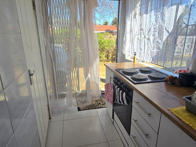 Compact kitchen area featuring tiled flooring, wall tiling, a built-in oven with electric hob, and a wooden countertop, with direct access to the exterior.