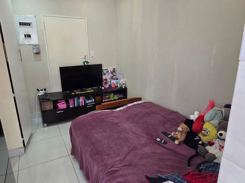 A compact bedroom featuring tiled flooring and a wall-mounted electrical distribution board.