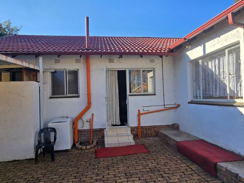 Rear exterior view of the property featuring a paved courtyard, tiled roof, and external access points with security gates.