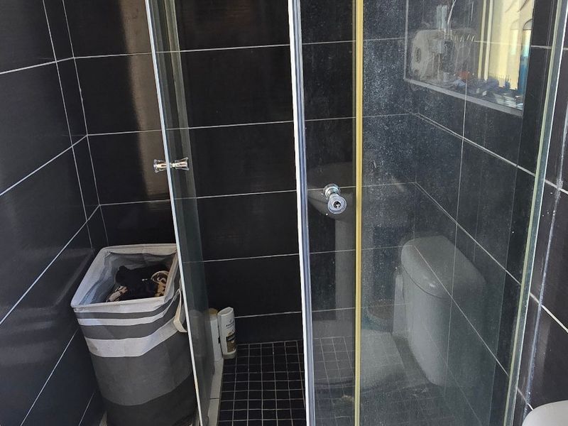 A compact bathroom featuring a shower enclosure with black wall and floor tiling, paired with a standard toilet.