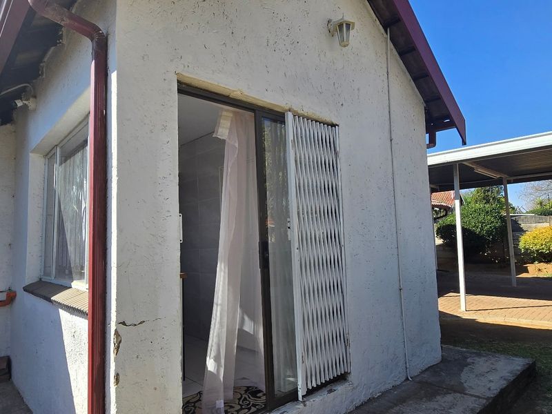 Rear exterior view of the property featuring a sliding glass door with security gate, tiled roof, and adjacent carport structure.