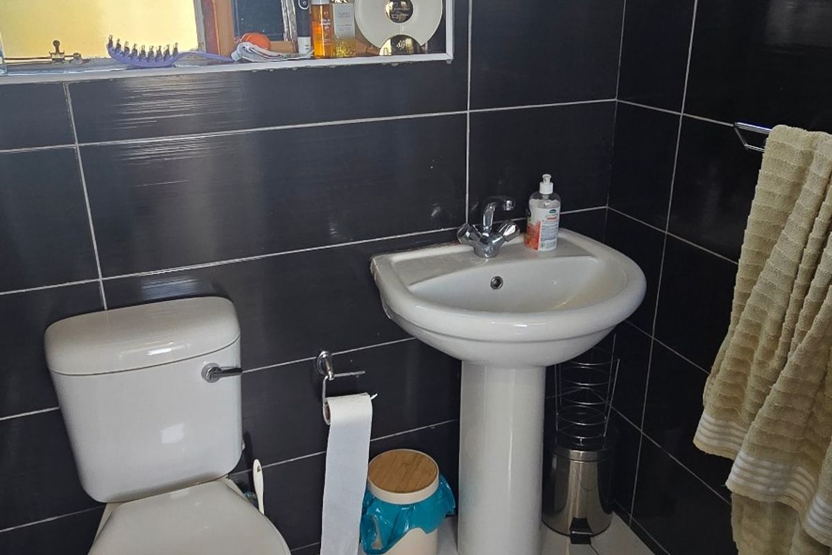 A compact bathroom featuring a pedestal basin, toilet, and dark tiled walls with contrasting white floor tiles.