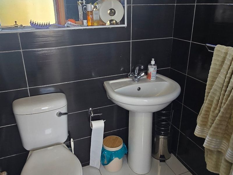 A compact bathroom featuring a pedestal basin, toilet, and dark tiled walls with contrasting white floor tiles.
