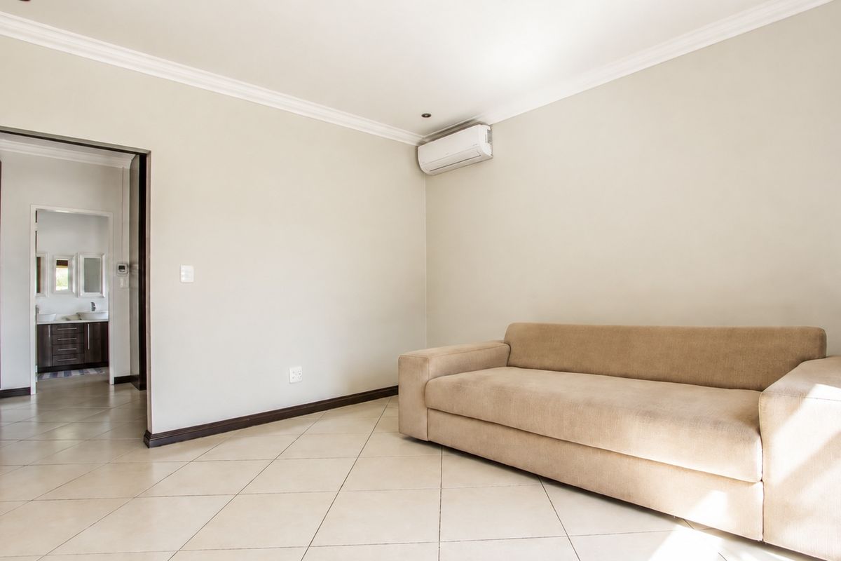 A well-maintained bedroom featuring tiled flooring, built-in cupboards, and an air conditioning unit, with an adjoining en-suite bathroom visible through the doorway.
