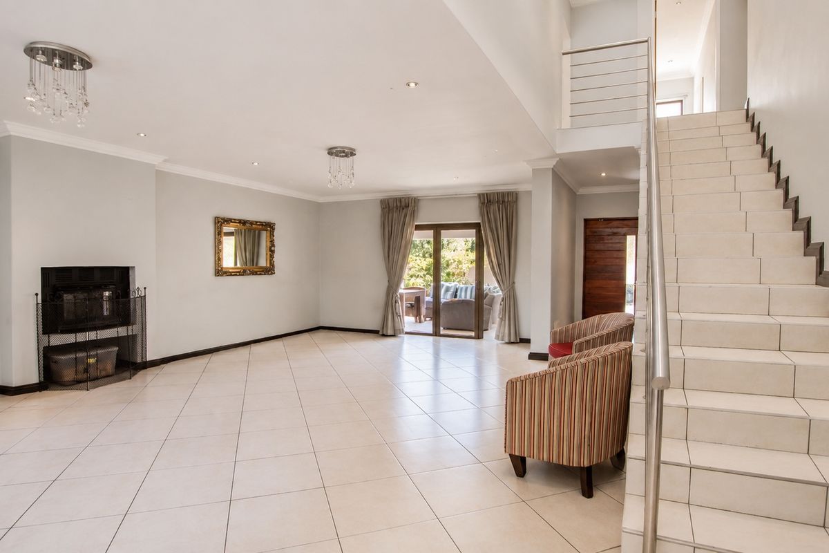 Spacious open-plan living area featuring tiled floors, a built-in fireplace, and a modern staircase leading to the upper level with access to the patio.