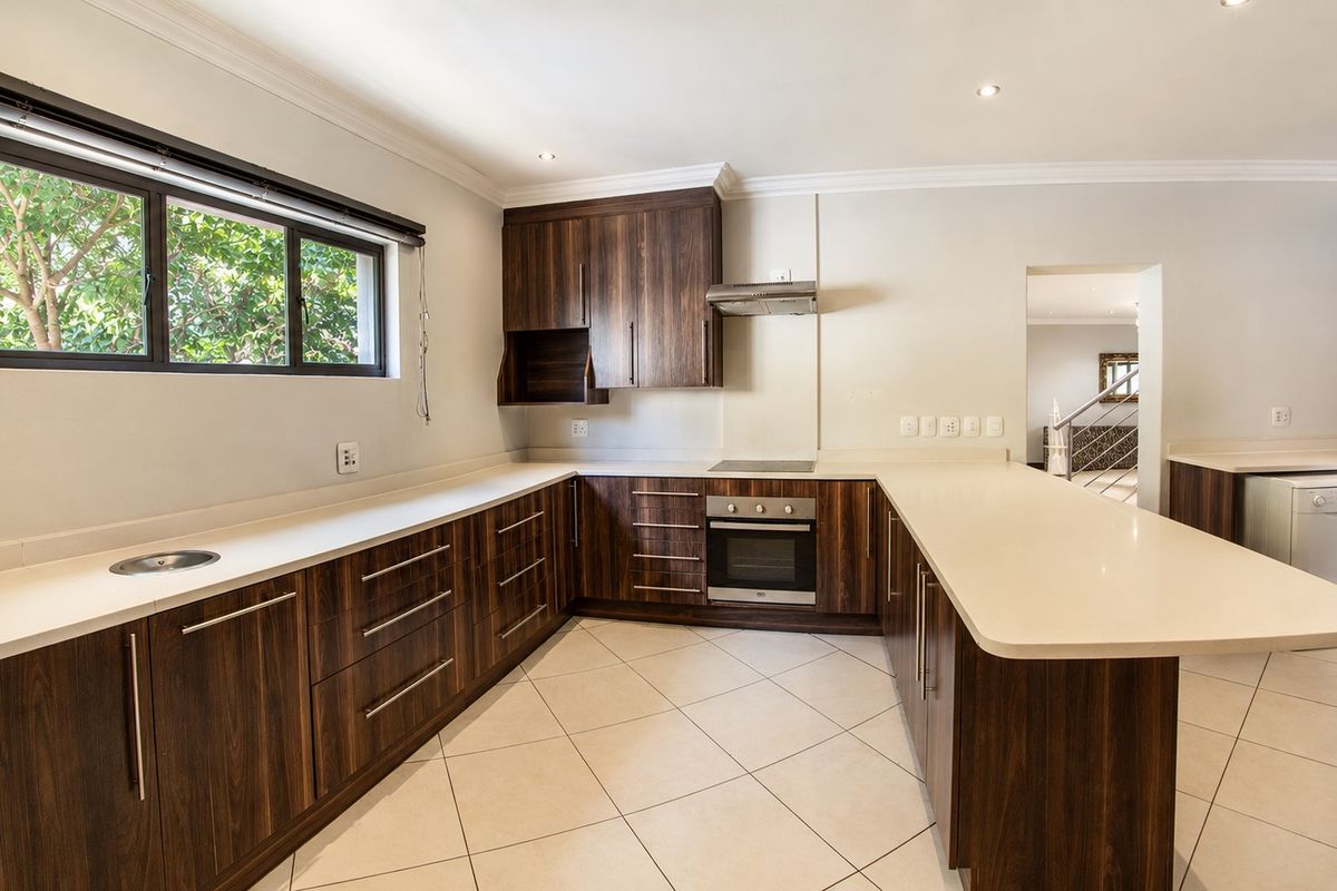 A modern, well-maintained kitchen featuring dark wood cabinetry, light stone countertops, integrated oven and hob, and tiled flooring in an open-plan layout.