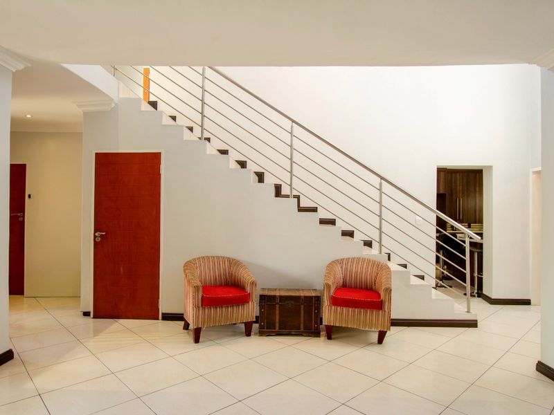 Spacious entrance hall featuring a modern staircase with stainless steel balustrades and neutral tiled flooring throughout.