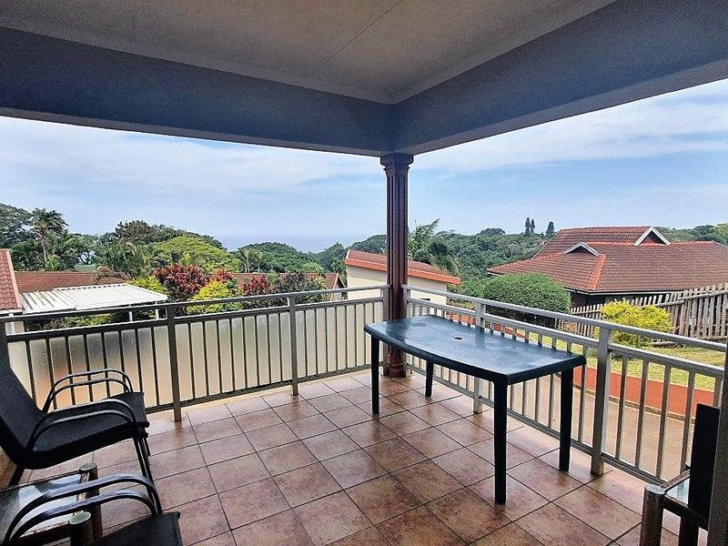 A covered balcony featuring tiled flooring and a metal balustrade, offering scenic views of the surrounding neighborhood and greenery.