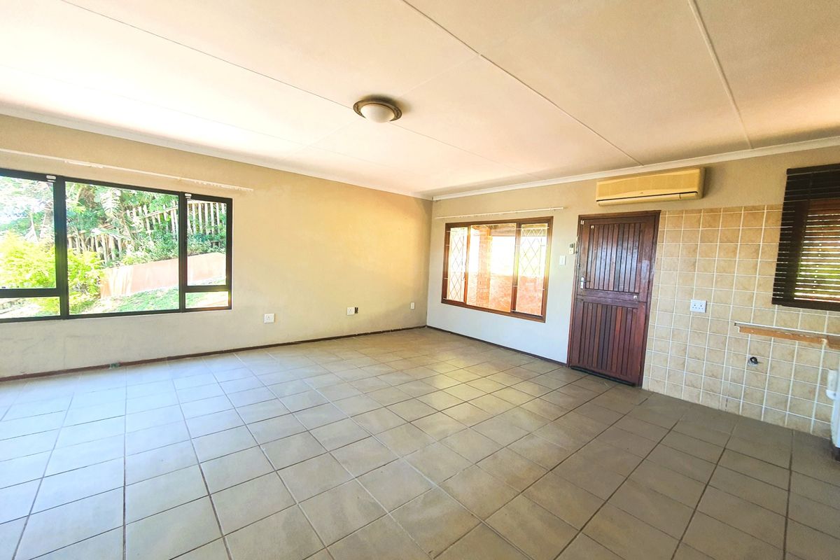 An empty, open-plan living area featuring tiled flooring, a wall-mounted air conditioning unit, and large windows providing natural light.
