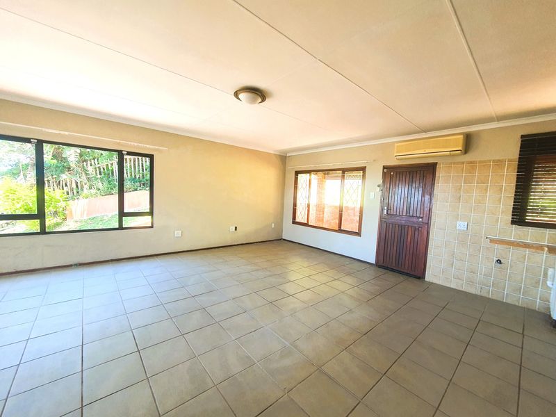 An empty, open-plan living area featuring tiled flooring, a wall-mounted air conditioning unit, and large windows providing natural light.