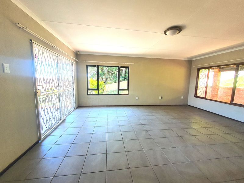 A spacious, empty living area featuring neutral tiled flooring, large windows, and a sliding glass door with a security gate.