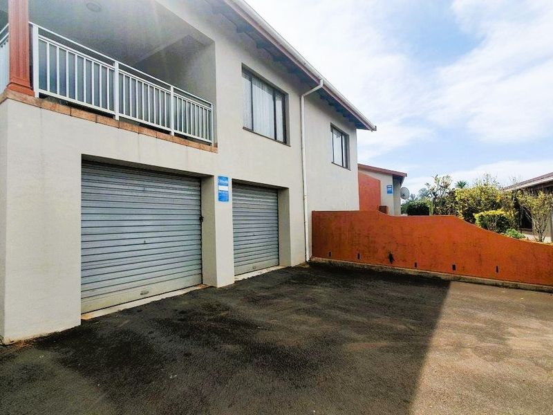 Exterior view of a townhouse featuring a double garage with roller shutter doors, an upper-level balcony with metal railings, and an external staircase.