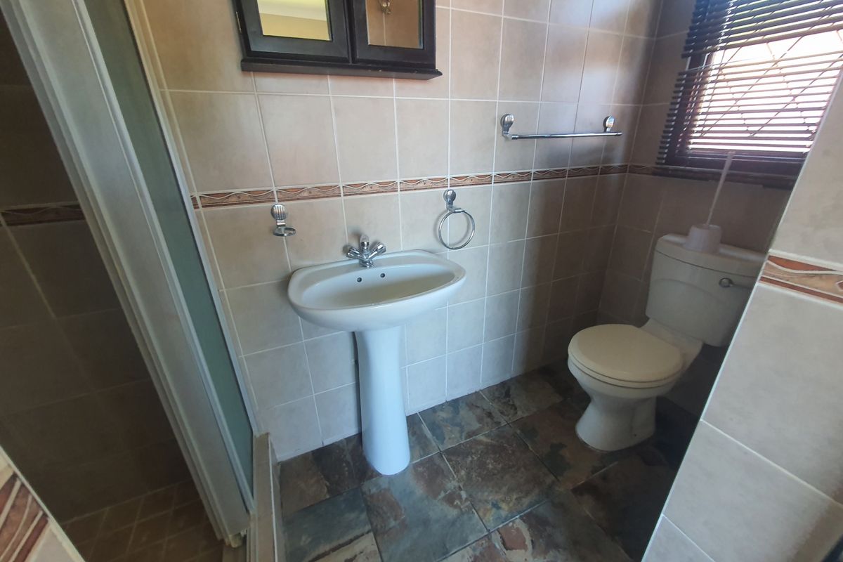 A functional bathroom featuring a pedestal basin, toilet, and shower enclosure with tiled walls and flooring.