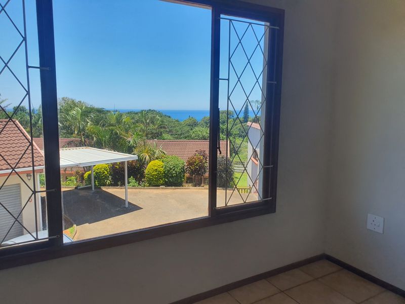 An interior view from a room featuring tiled flooring and security bars on the window, overlooking a coastal landscape and residential area.