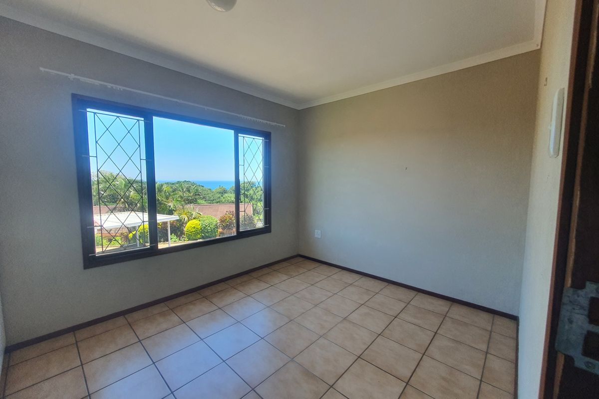 An empty bedroom featuring tiled flooring, neutral walls, and a large window with security bars offering a pleasant outdoor view.