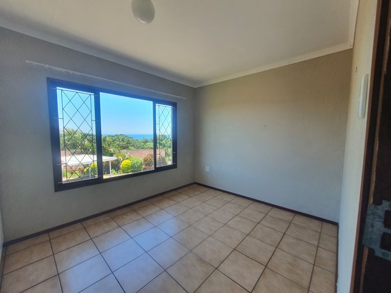 An empty bedroom featuring tiled flooring, neutral walls, and a large window with security bars offering a pleasant outdoor view.
