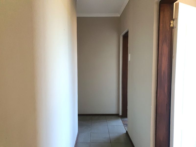 A simple, empty interior hallway featuring tiled flooring and wooden door frames, providing access to other rooms within the townhouse.