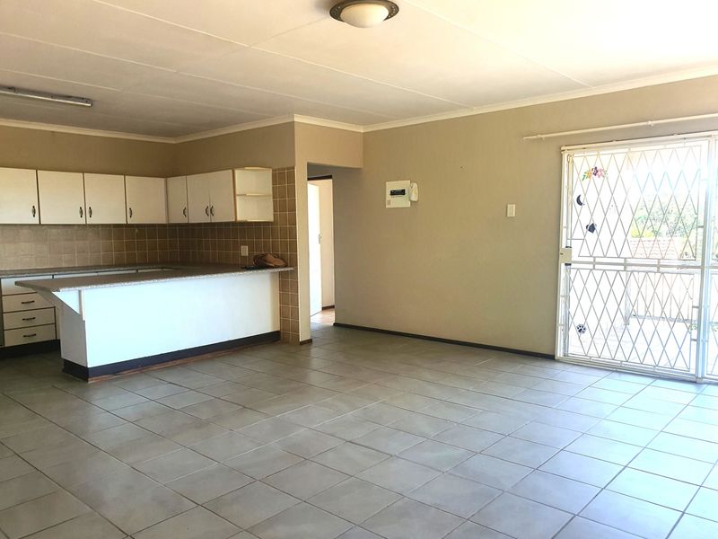 Spacious open-plan living area featuring a functional kitchen with built-in cabinetry and tiled flooring, leading to a secure sliding door entrance.