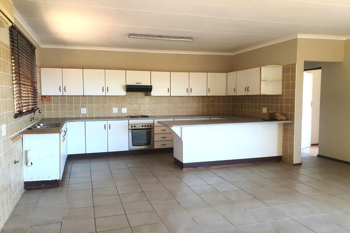 Spacious kitchen featuring white built-in cabinetry, laminate countertops, integrated oven, extractor fan, and tiled flooring, offering a functional layout ready for modernization.