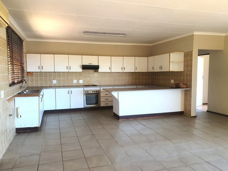 Spacious kitchen featuring white built-in cabinetry, laminate countertops, integrated oven, extractor fan, and tiled flooring, offering a functional layout ready for modernization.
