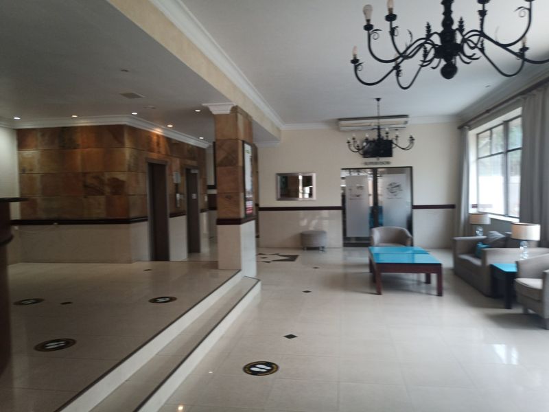 Spacious apartment building lobby featuring tiled flooring, stone-clad accent walls, elevator access, and decorative wrought iron chandeliers.
