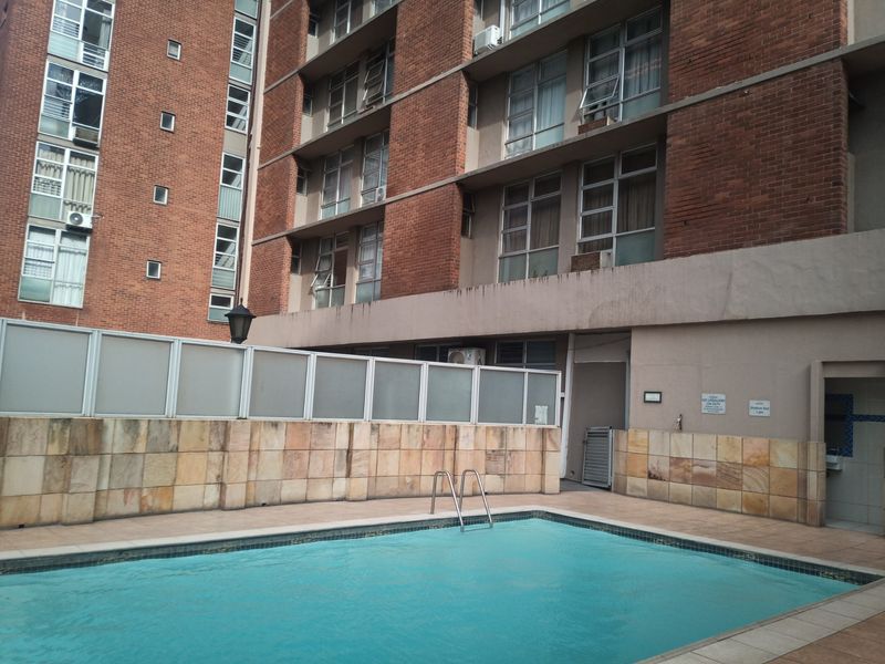 Communal swimming pool area featuring stone-clad walls, privacy screening, and direct access to the apartment building's brick facade.