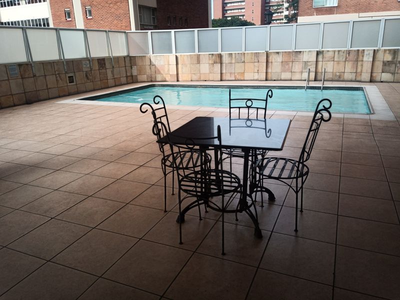 A communal outdoor pool area featuring a tiled deck, stone wall cladding, and metal privacy screens, providing a functional space for residents.