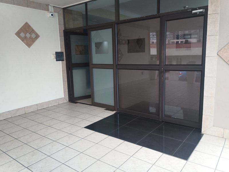 A secure apartment building entrance featuring tiled flooring and aluminium framed glass doors with an integrated security intercom system.