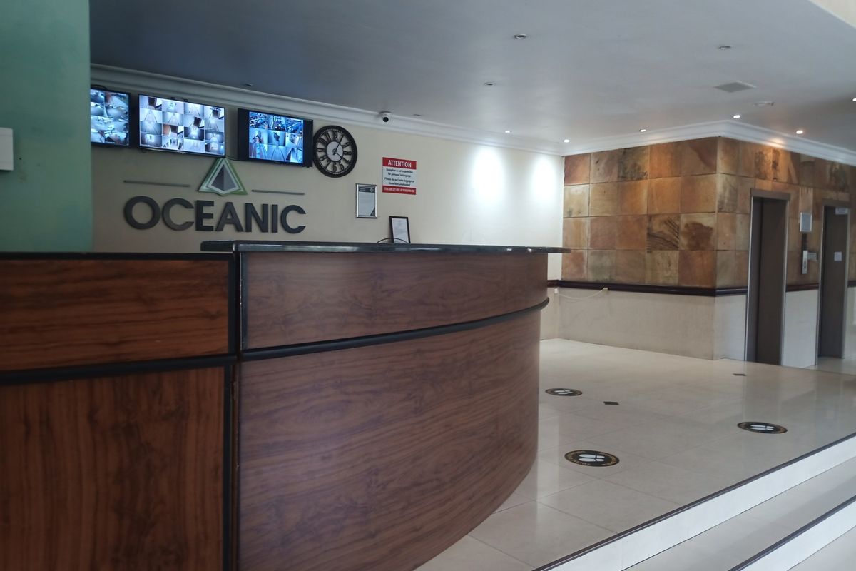 A professional apartment building lobby featuring a reception desk, security monitoring system, and elevator access with stone wall accents.