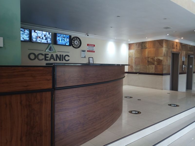 A professional apartment building lobby featuring a reception desk, security monitoring system, and elevator access with stone wall accents.