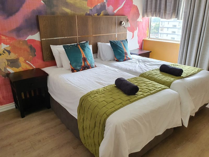 A bedroom featuring laminate flooring, a built-in wooden headboard, and a large floral feature wall.