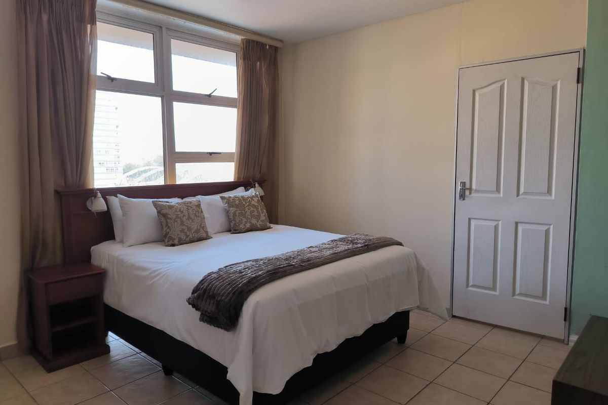 A functional bedroom featuring tiled flooring, a built-in headboard, and a large window providing natural light.