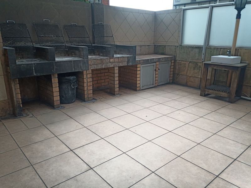 Outdoor patio area featuring a large built-in brick braai station, tiled flooring, and a dedicated outdoor sink area.
