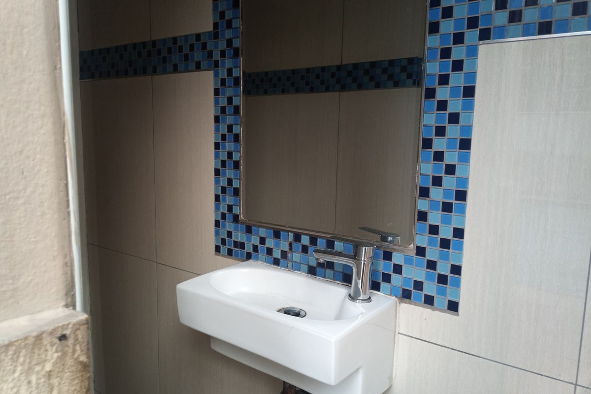 A compact bathroom vanity area featuring a wall-mounted basin, chrome mixer tap, and decorative blue mosaic tile accents.