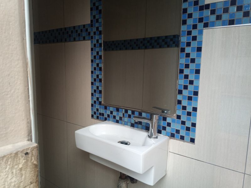 A compact bathroom vanity area featuring a wall-mounted basin, chrome mixer tap, and decorative blue mosaic tile accents.