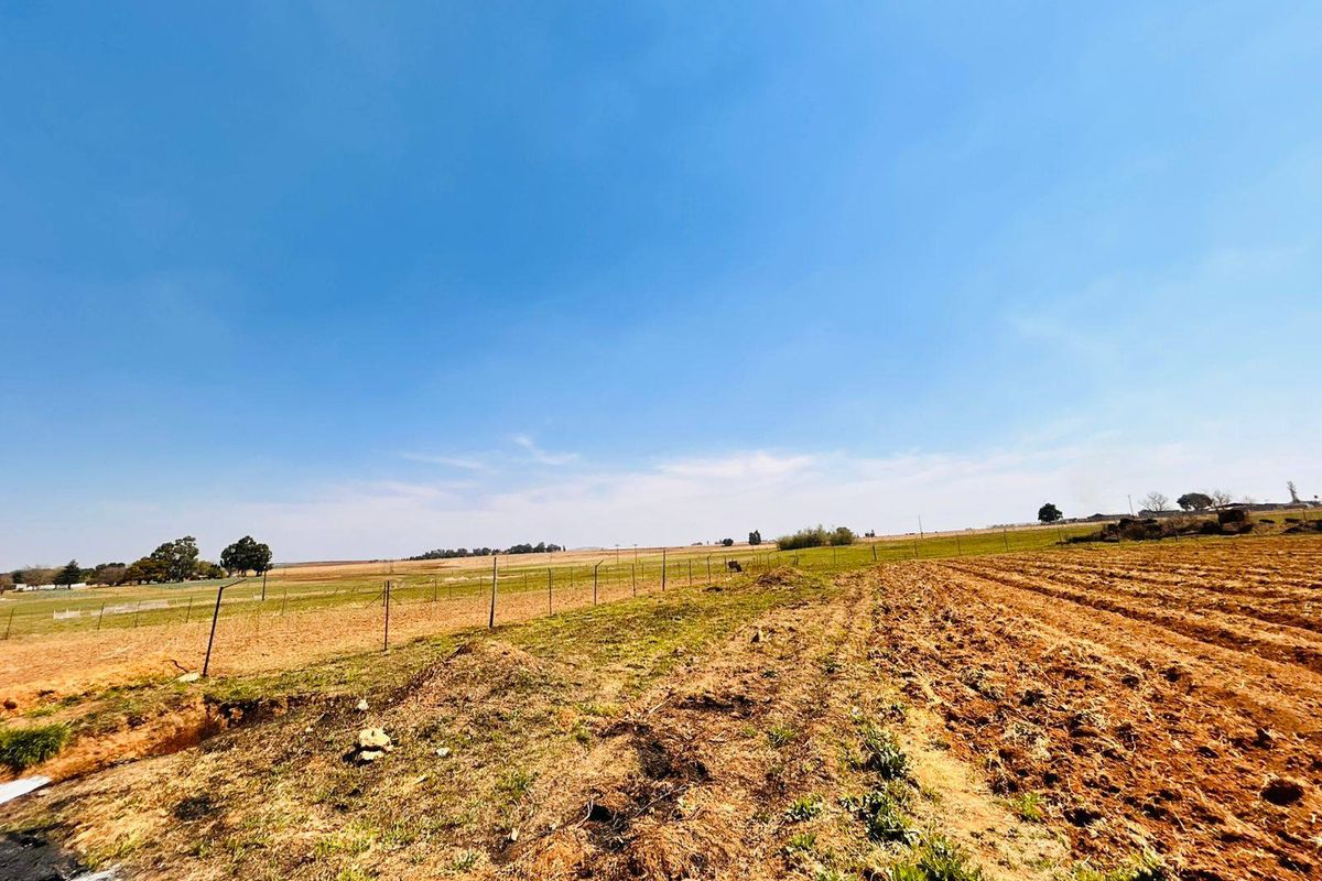 A wide-angle view of open farmland featuring cultivated soil and wire perimeter fencing under a clear blue sky.