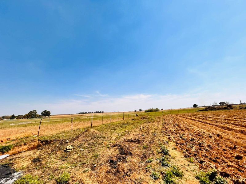 A wide-angle view of open farmland featuring cultivated soil and wire perimeter fencing under a clear blue sky.