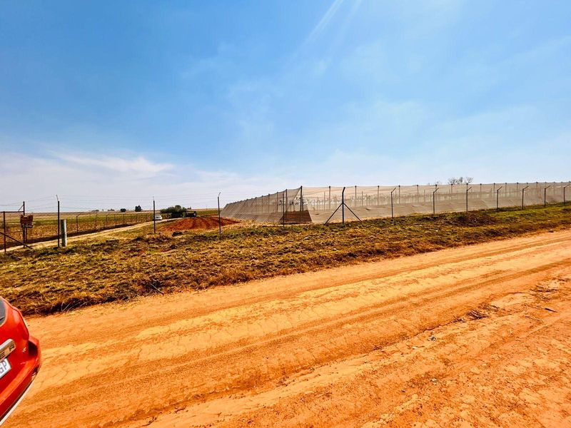 View of a fenced agricultural plot with protective netting, situated alongside a dirt access road on the farm property.