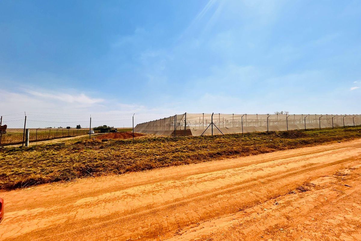 A view of the farm property featuring extensive perimeter fencing and agricultural netting structures set against a rural landscape.