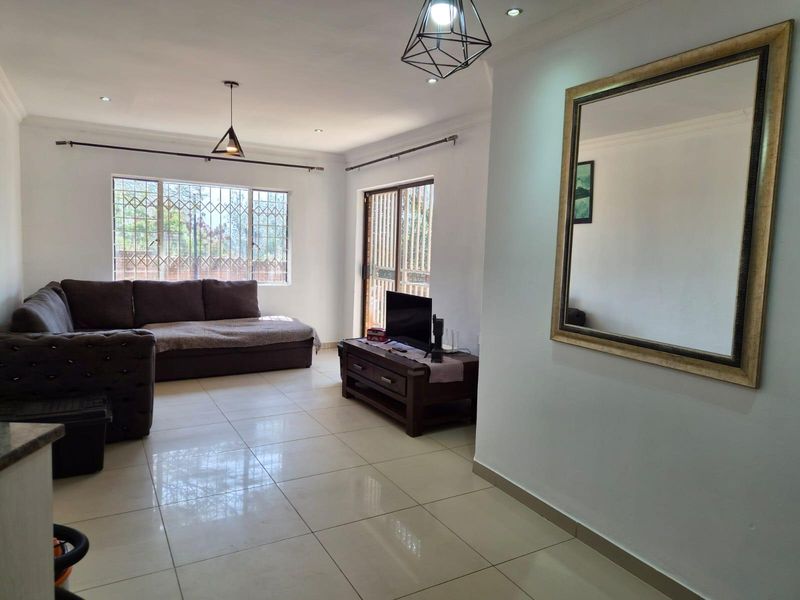 A bright and spacious living room featuring large windows with security bars, tiled flooring, and modern pendant lighting, offering a comfortable and functional living space.