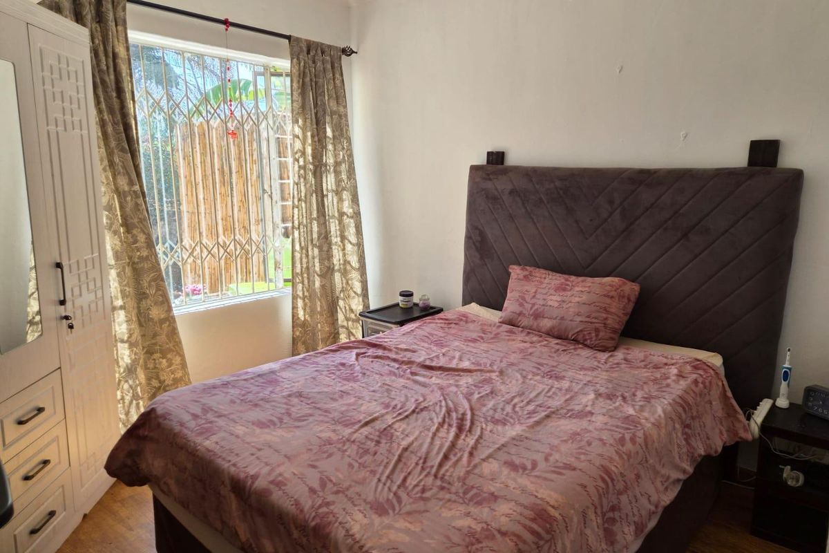 A functional bedroom featuring laminate flooring, a built-in wardrobe, and a window fitted with a security gate.