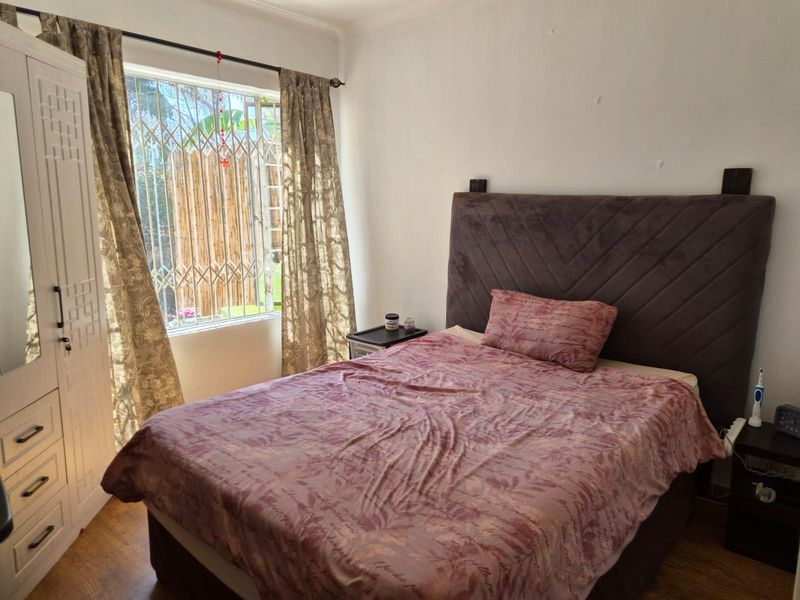 A functional bedroom featuring laminate flooring, a built-in wardrobe, and a window fitted with a security gate.