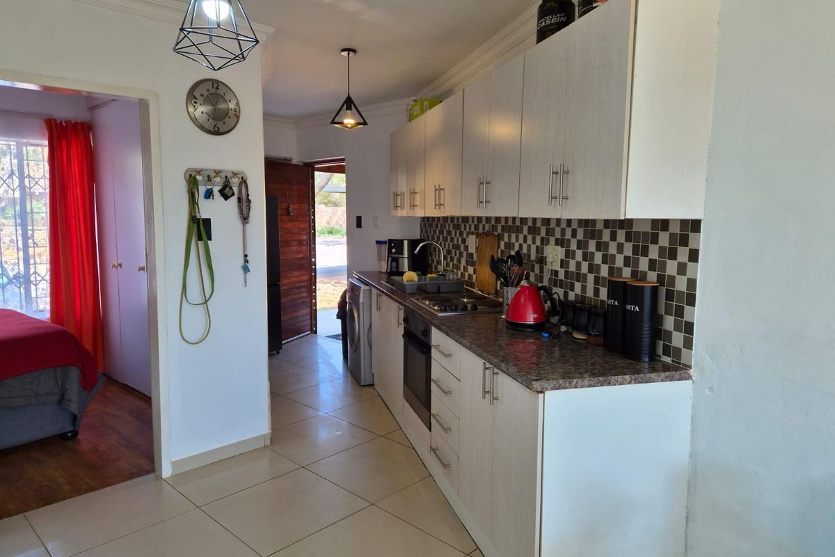 A functional galley-style kitchen featuring light-toned cabinetry, dark laminate countertops, a tiled backsplash, and integrated cooking appliances with tiled flooring throughout.
