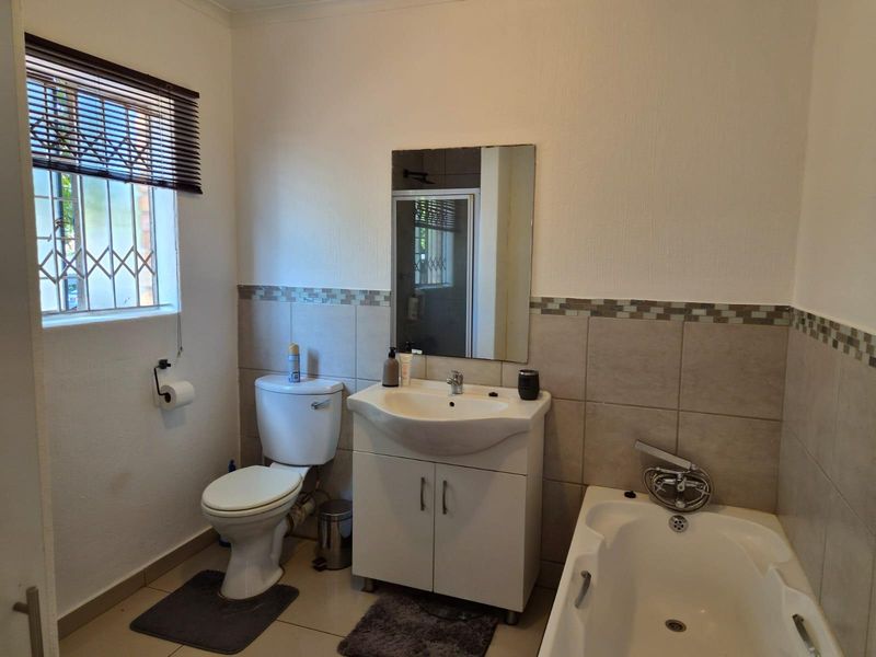 A functional bathroom featuring a vanity cabinet, basin, toilet, and bathtub with neutral wall tiling and security bars on the window.