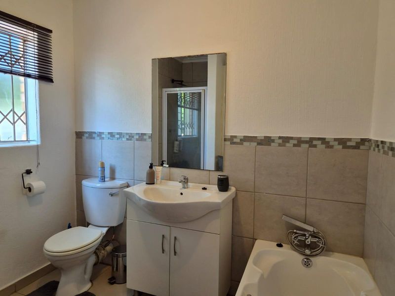 A functional bathroom featuring a vanity cabinet, basin, toilet, and bathtub with a handheld shower mixer, finished with neutral wall tiling.