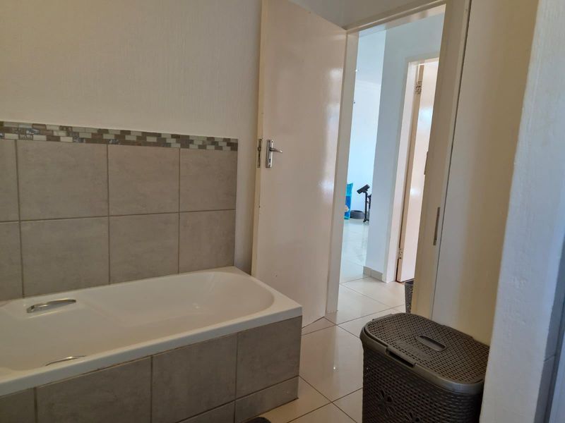 A functional bathroom featuring a built-in bathtub with neutral wall tiling and ceramic floor tiles, leading into a hallway.