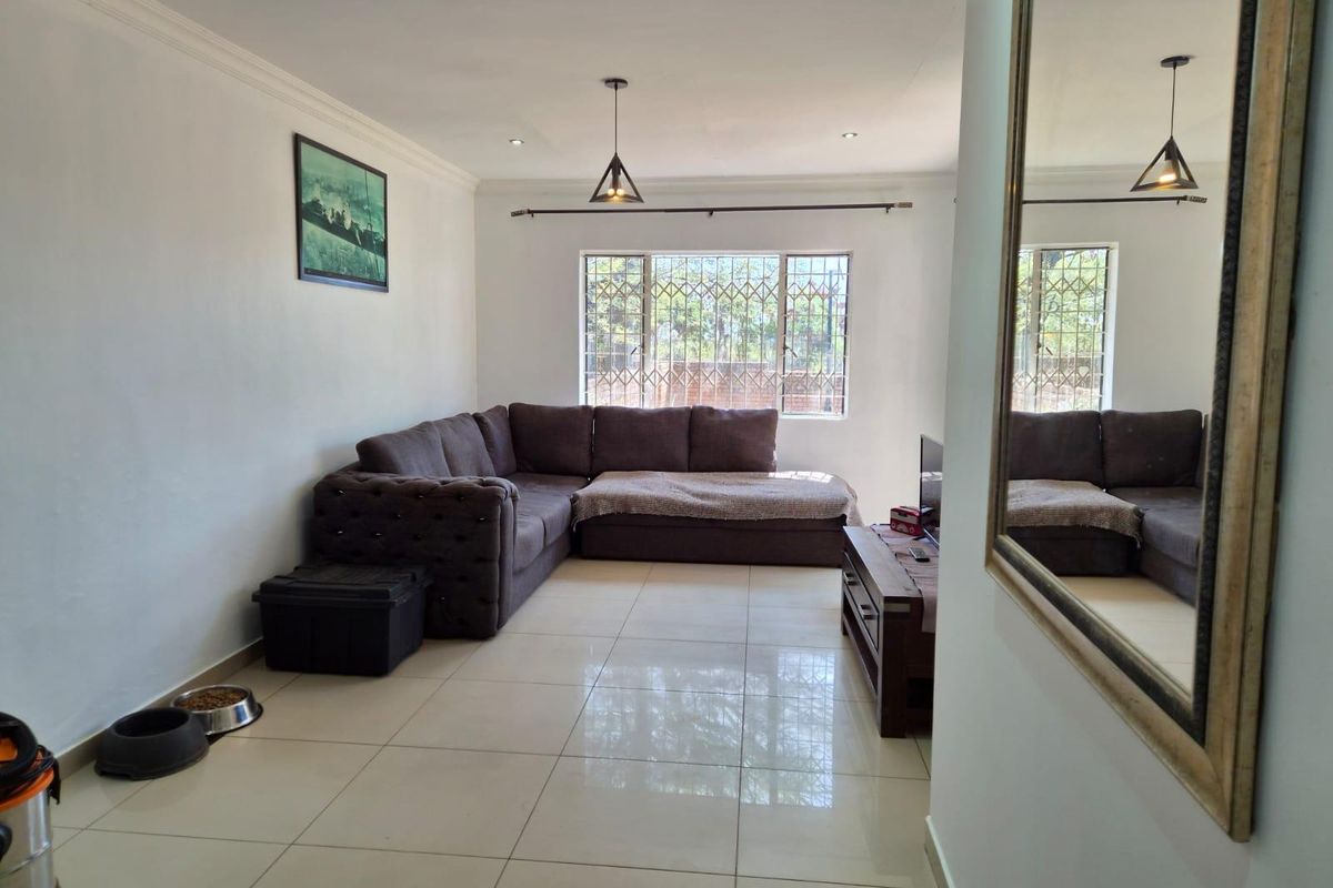 A well-maintained living room featuring large format floor tiles, recessed downlighting, and security bars on the windows, providing a clean and functional living space.